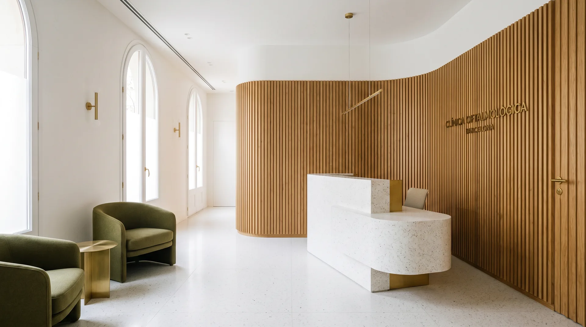 Recepción de Clínica Llum con madera de roble, terrazo blanco y butacas verde oliva